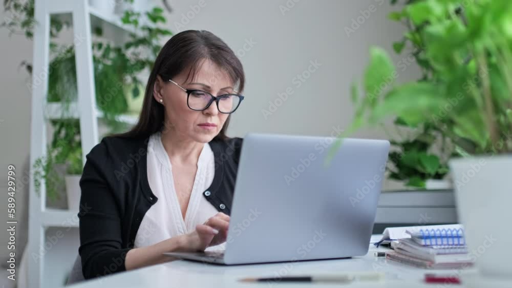 Serious middle aged woman working in home office, typing on laptop Serious middle aged woman working in home office, typing on laptop