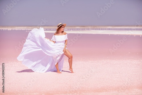 Woman in pink salt lake. She walks in a white long dress and hat along the salty white shore of the lake. Wanderlust photo for memory