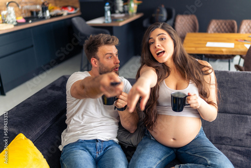 a young couple, parents-to-be, are watching a movie and commenting passionately, pointing their hands at the camera and having a fun time