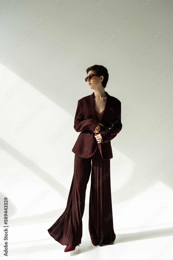 full length of brunette woman in sunglasses and elegant pantsuit grey background with lighting. full length of brunette woman in sunglasses and elegant pantsuit grey background with lighting.
