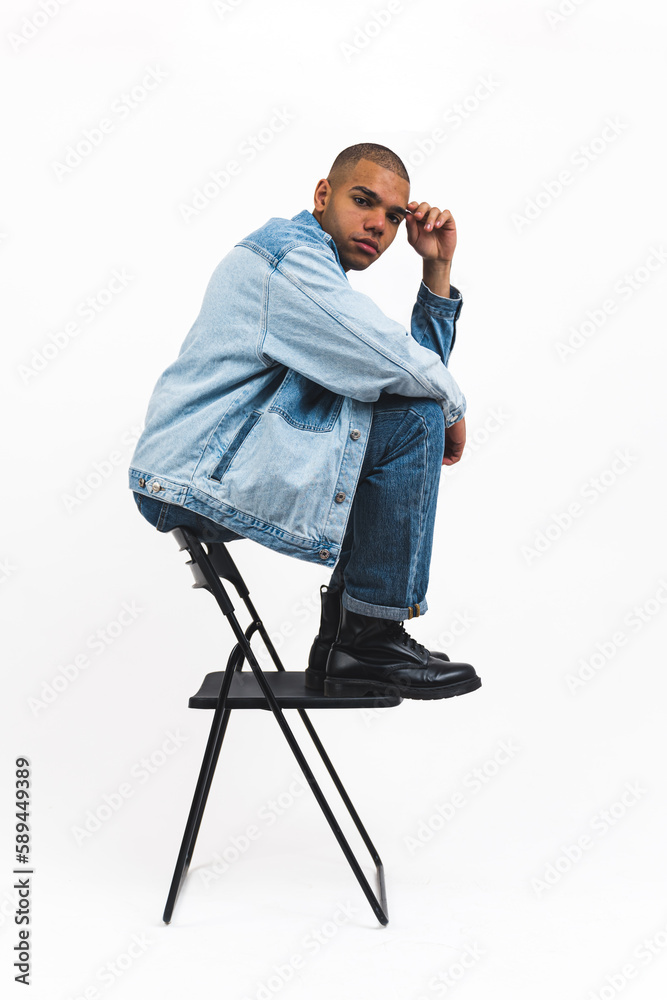 African American male model in full denim outfit sitting on top of a folding chair on white background . High quality photo African American male model in full denim outfit sitting on top of a folding chair on white background . High quality photo