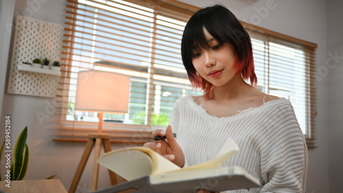 Concentred asian female freelancer reading literature or checking her working schedule plan on diary