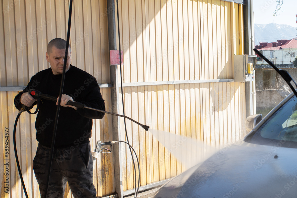 self car wash, a man washes a car with a hose at a self-service station self car wash, a man washes a car with a hose at a self-service station