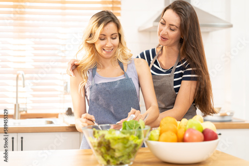 happy and smile lesbian couple cooking salad in the kitchen. salad in glass bowl with sweet smile while cooking together. pride month to promote equality and differences of homosexual.