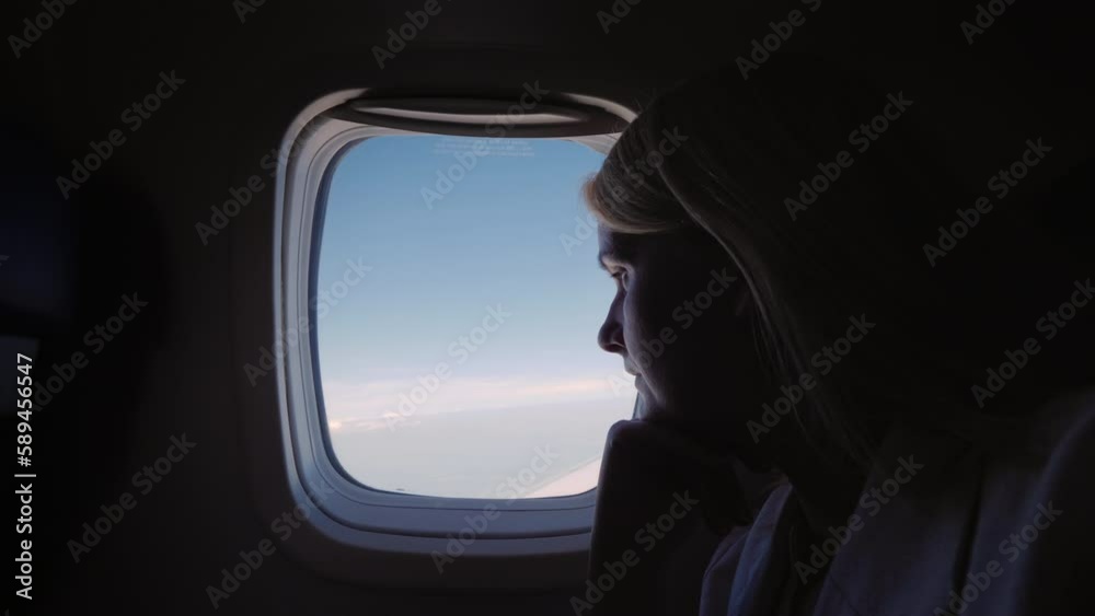 Silhouette of a young woman flying in an airplane, looking out the window Silhouette of a young woman flying in an airplane, looking out the window