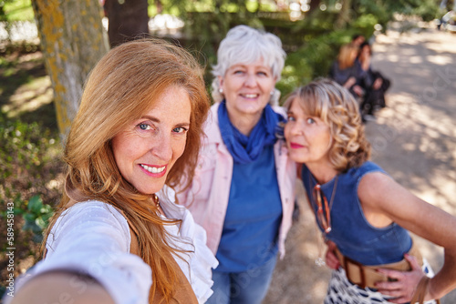 Cheerful trio of ladies having fun while taking a group selfie with a cell phone.