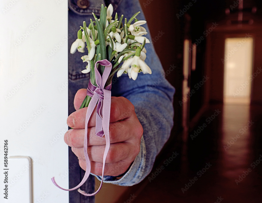 Bouquet of snowdrops in the hand of a man hiding behind a door, close-up