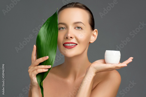 Organic skin detox. Beauty face portrait of young woman is posing with a green tropical leaf and jare of cream or cosmetic product . Natural cosmetic and facial treatment. Skincare and hydration. photo