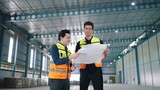 Two professional engineer male worker talking and discuss to work holding and looking at paper work in factory Industrial