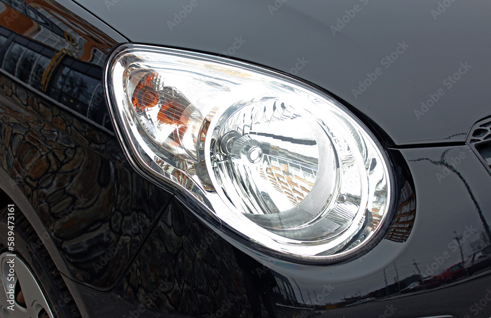 Close-up front headlight with xenon light of black modern car.