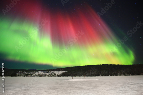 Red and green aurora above frozen lake in northern Sweden