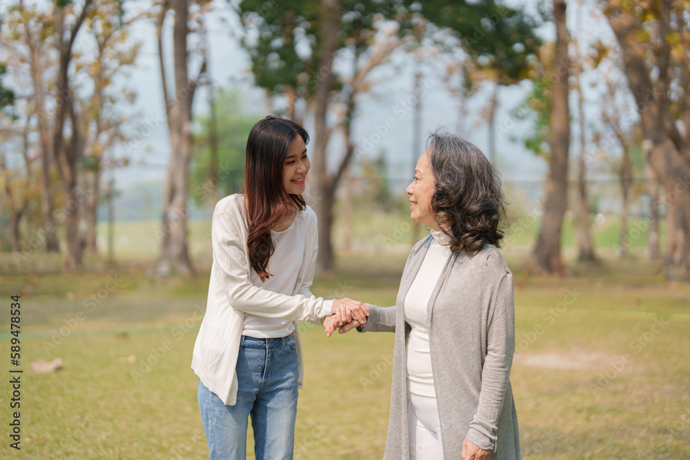 Adult daughter holding her elderly mother hand with love and walk together in park Adult daughter holding her elderly mother hand with love and walk together in park