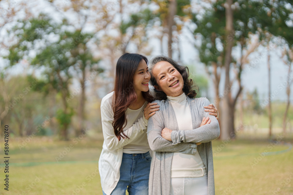 Grown daughter with aging mother showing love and walking together in the parkland Grown daughter with aging mother showing love and walking together in the parkland