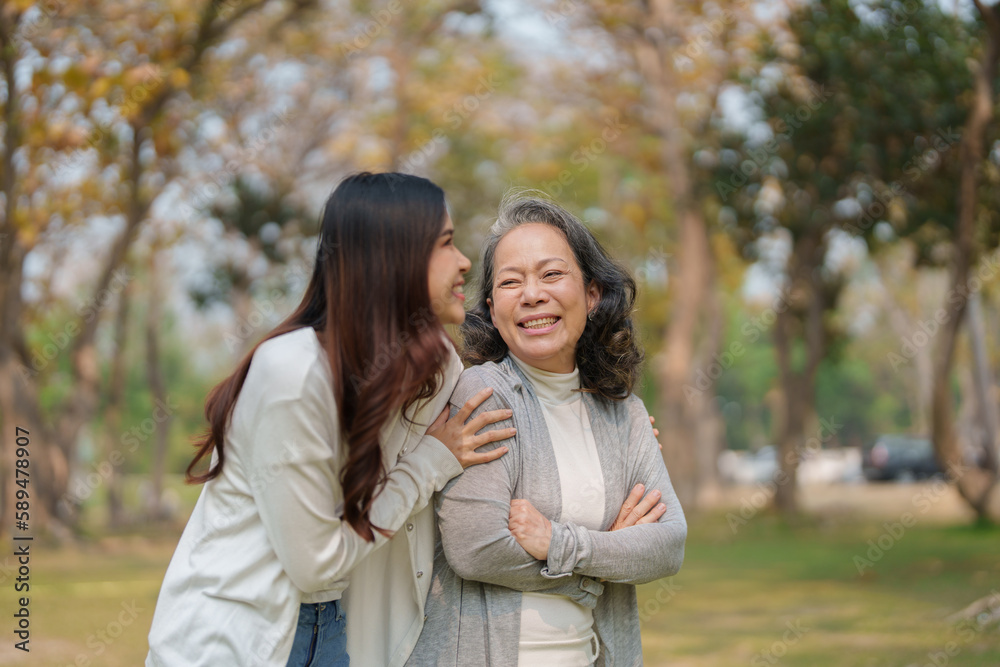 Grown daughter with aging mother showing love and walking together in the parkland Grown daughter with aging mother showing love and walking together in the parkland