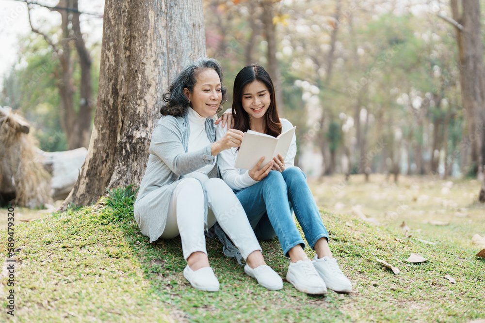 Fototapeta premium Grown daughter with aging mother expressing love and looking at memory notebook under tree in public park