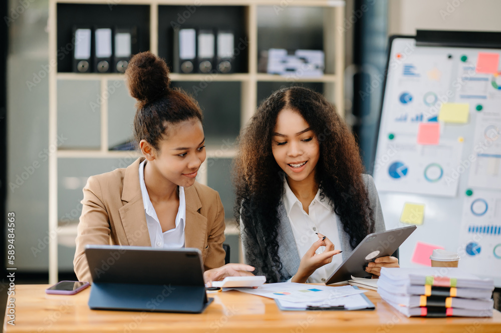 Two African businesswoman discuss investment project working and planning strategy with tablet laptop computer in office.
