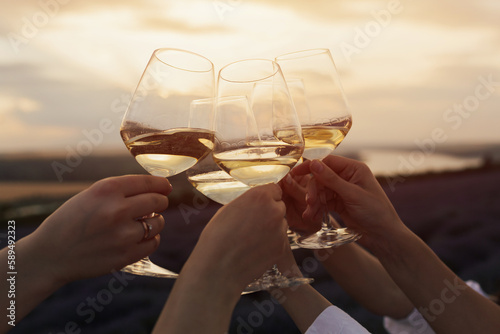 Close-up of hands with glasses of white wine at sunset. People raised their glasses. Friends clinking glasses with wine.