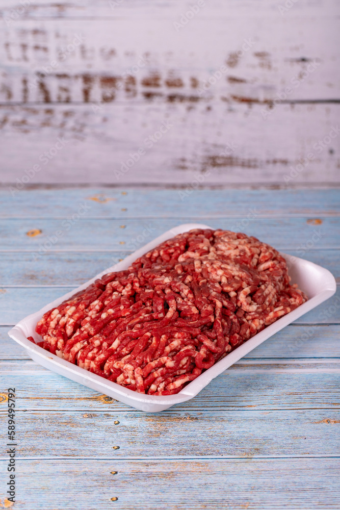 Raw ground beef in a white polystyrene tray on a wood background. Fresh ground beef on wood background. Raw ground beef in a white polystyrene tray on a wood background. Fresh ground beef on wood background.