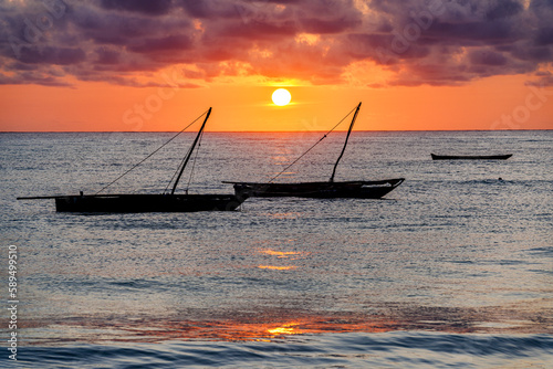 Cloudy sky at sunrise over silhouettes of boats moored in the sea, Jambiani, Zanzibar, Tanzania photo