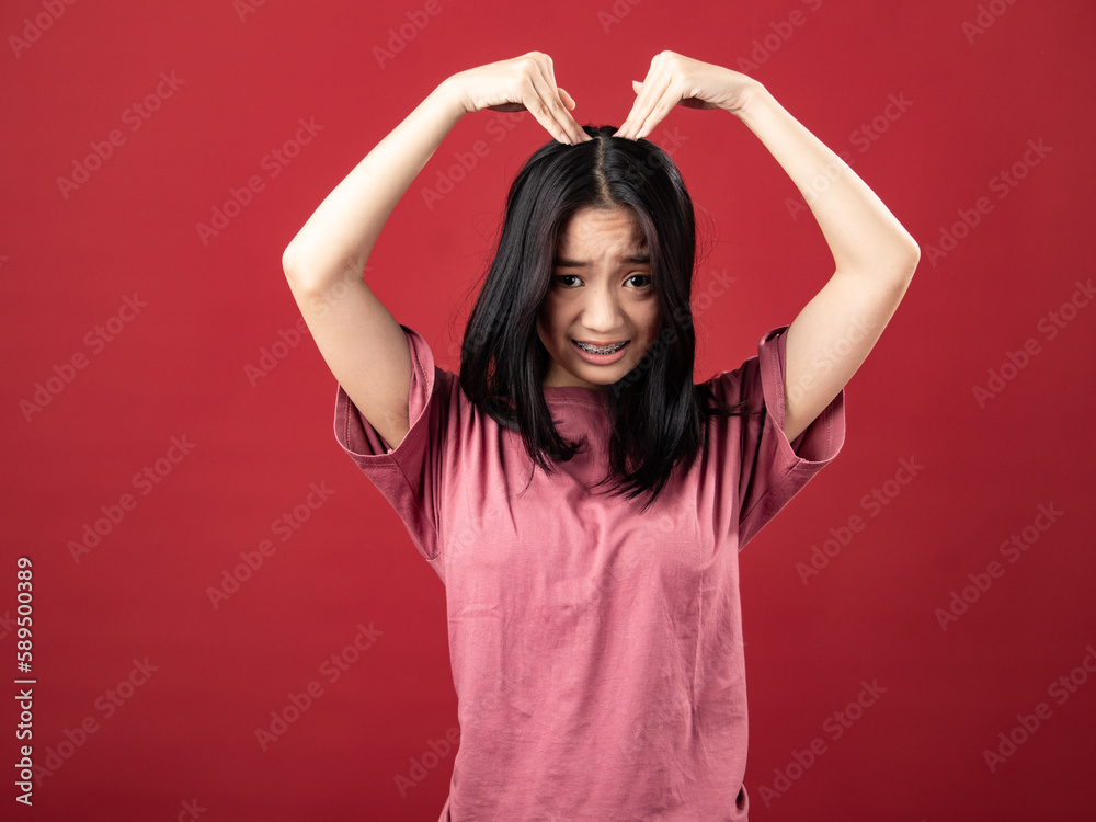 A portrait of a young Indonesian (Asian) woman wearing a pink shirt, making a heart sign with both hands connected above her head. Isolated with a red background A portrait of a young Indonesian (Asian) woman wearing a pink shirt, making a heart sign with both hands connected above her head. Isolated with a red background