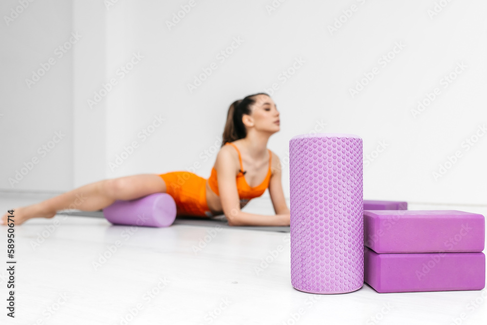 Fit athletic women in sportswear ride on a pink foam myofascial massage roller, massaging their muscles on the floor of a yoga mat in the gym. Active girls do a fitness workout in the gym. MFR Fit athletic women in sportswear ride on a pink foam myofascial massage roller, massaging their muscles on the floor of a yoga mat in the gym. Active girls do a fitness workout in the gym. MFR