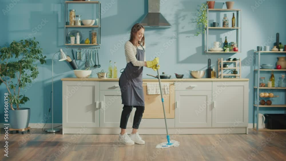 Creative Woman is Washing Floor With Mop and Dancing in Kitchen at Home.Happy Young Woman Cute Housewife is Listening to Music and Dancing During Domestic Work. Household Chores Concept. Creative Woman is Washing Floor With Mop and Dancing in Kitchen at Home.Happy Young Woman Cute Housewife is Listening to Music and Dancing During Domestic Work. Household Chores Concept.