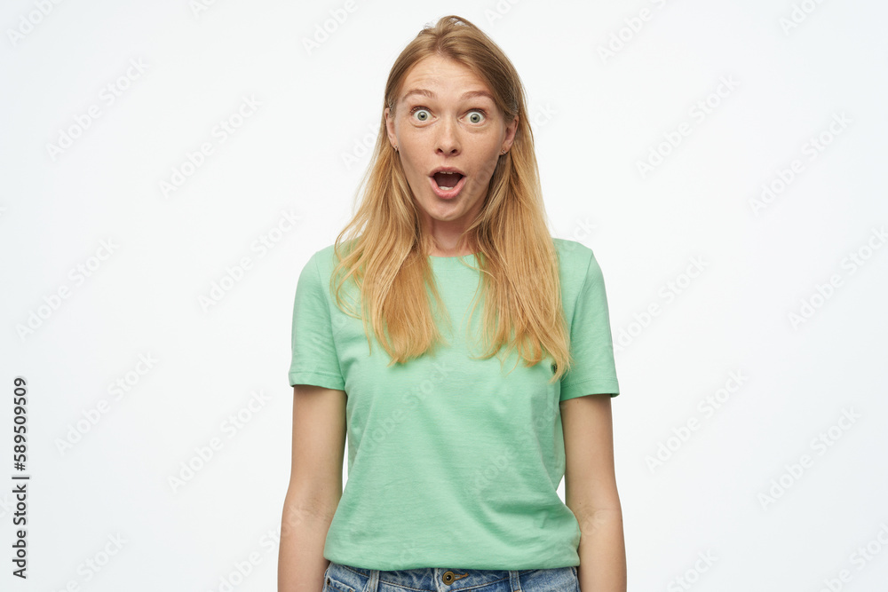 Indoor studio portrait of young ginger female with freckles looking into camera with shocked facial expression isolated over background Indoor studio portrait of young ginger female with freckles looking into camera with shocked facial expression isolated over background