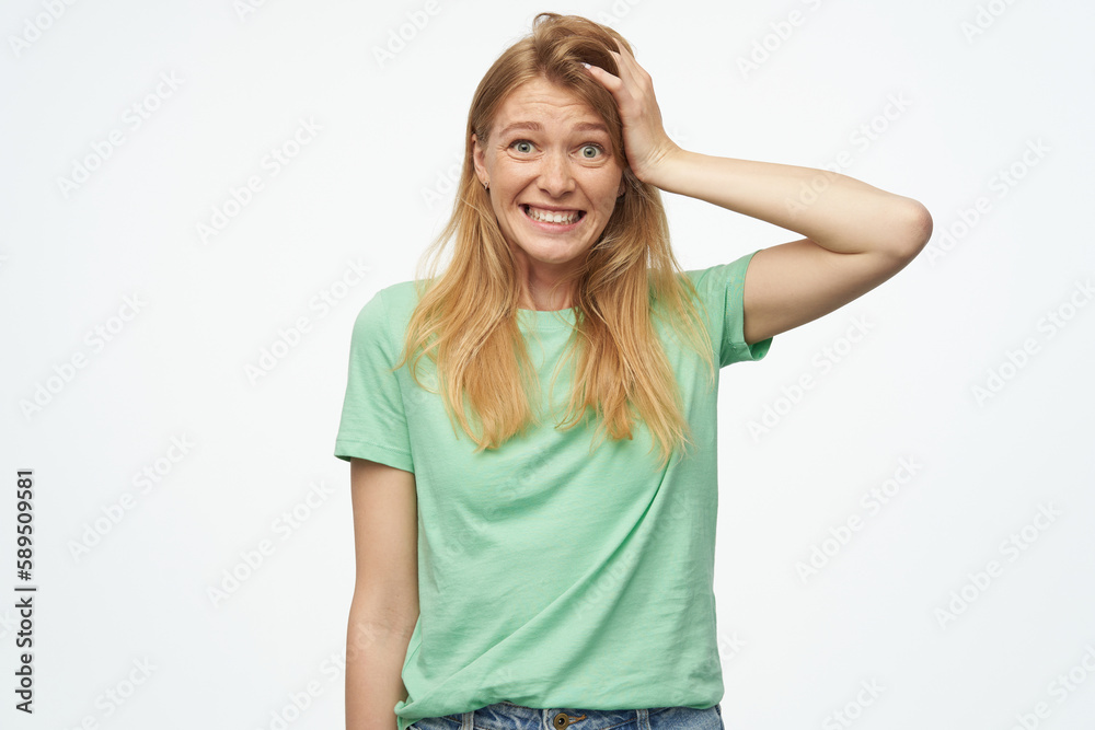 Indoor studio portrait of young ginger female with freckles points aside at copy space with finger isolated over background Indoor studio portrait of young ginger female with freckles points aside at copy space with finger isolated over background