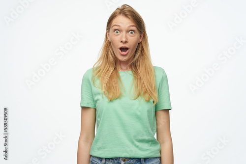 Indoor studio portrait of young ginger female with freckles looking into camera with shocked facial expression isolated over background © timtimphoto