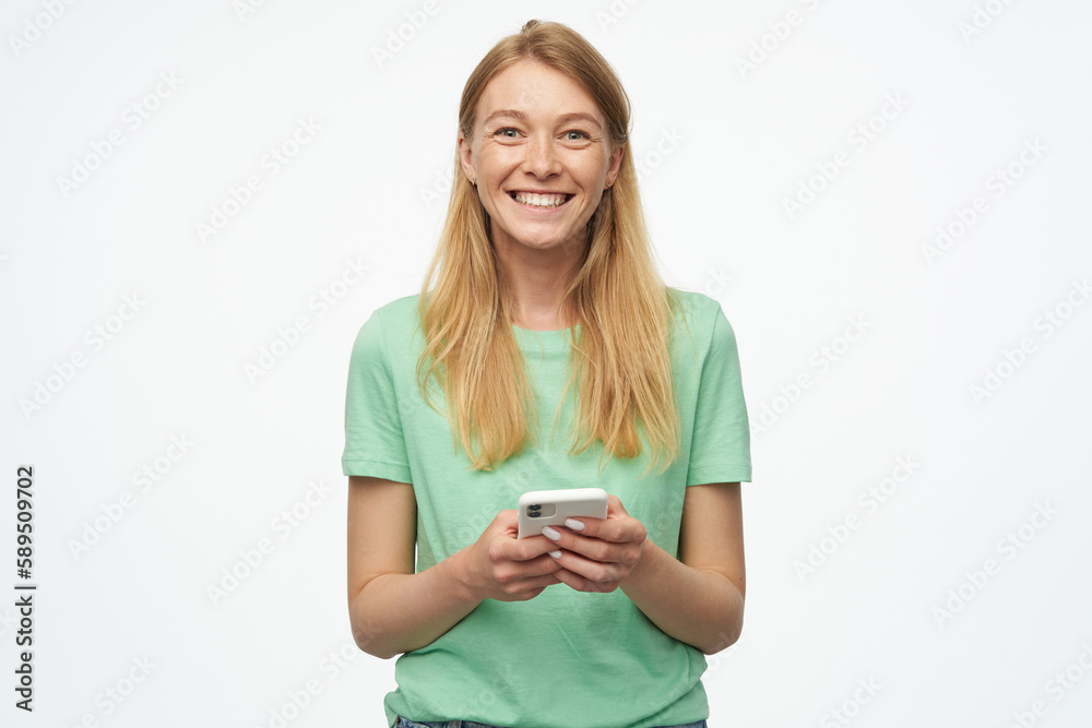 Indoor studio portrait of young ginger female with freckles typing message and smiles broadly isolated over background Indoor studio portrait of young ginger female with freckles typing message and smiles broadly isolated over background
