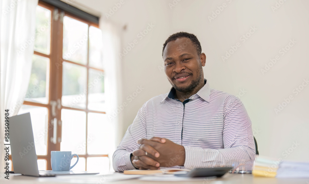Fototapeta premium Portrait of handsome African black young business man working on laptop at office desk.