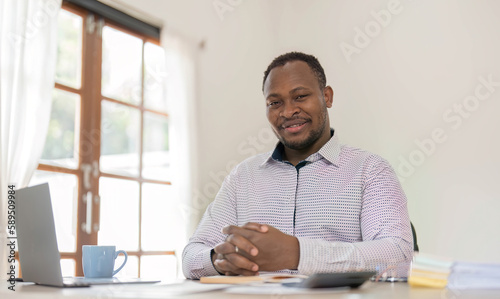 Portrait of handsome African black young business man working on laptop at office desk.
