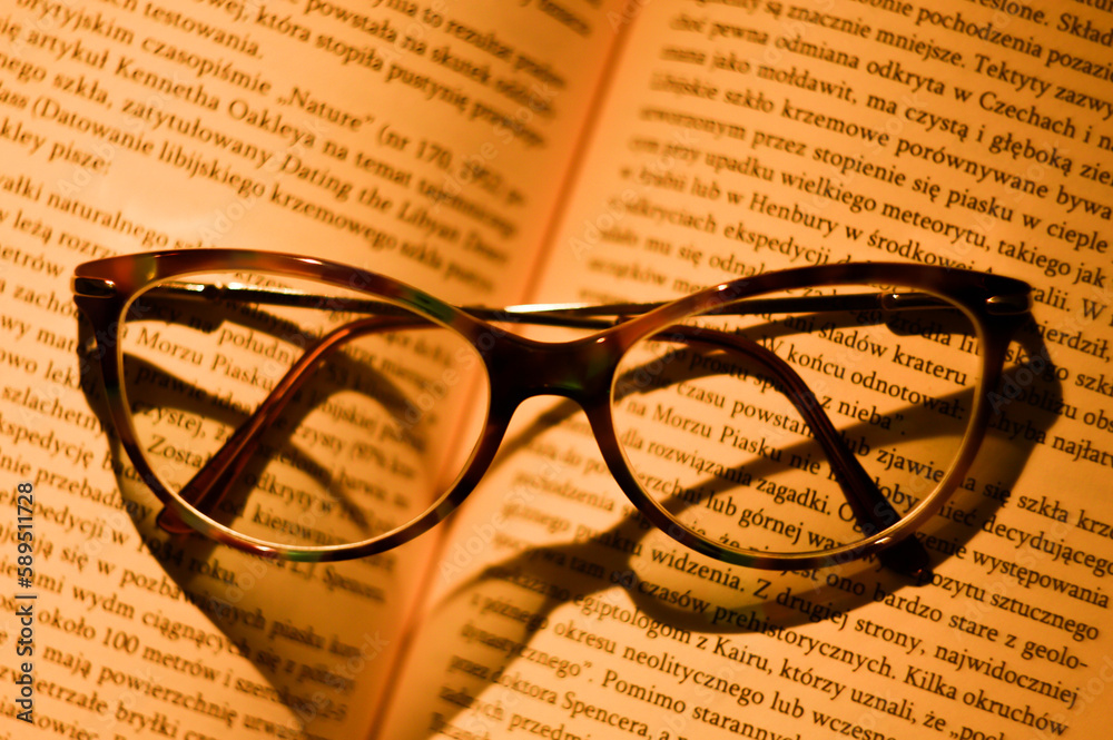 An open book and glasses lying on it isolated with warm light falling on it. An open book and glasses lying on it isolated with warm light falling on it.