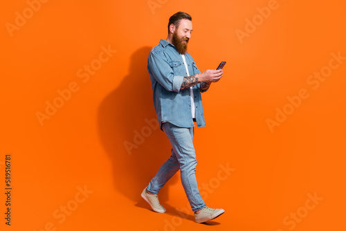 Profile side full body photo of millennial guy walking using gadget comment post isolated bright color background
