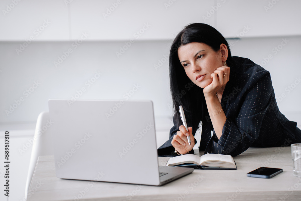 Pensive brunette tired businesswoman in suit works home sits at desk using laptop. Overloaded hispanic office manager unhappy watching news. Financial people, fatigue. Entrepreneur. Pensive brunette tired businesswoman in suit works home sits at desk using laptop. Overloaded hispanic office manager unhappy watching news. Financial people, fatigue. Entrepreneur.