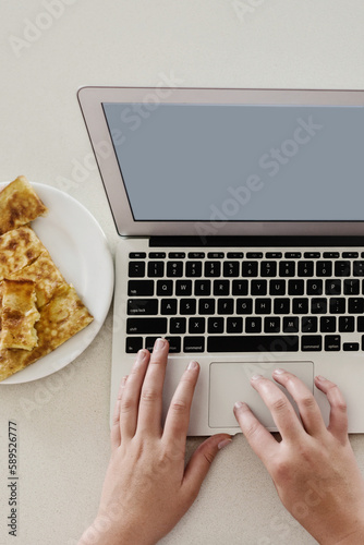 person typing on a laptop with grilled cheese snack photo