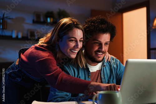 Murais de parede Young happy caucasian couple browsing on internet using a laptop to search sale at home