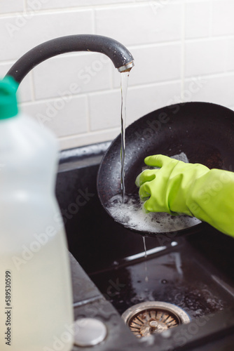 Person in Green Glove Washing Frying Pan with Sponge under Running Water from Tap in Kitchen