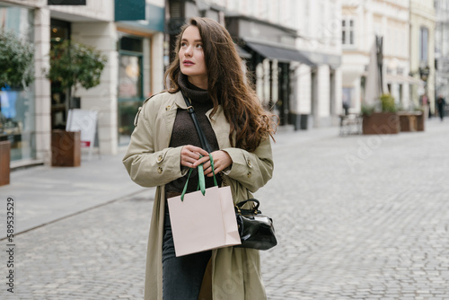 Fashion woman portrait of young pretty trendy girl posing at the city in Europe,summer street fashion, holding a blank shopping bag. Happy customer concept