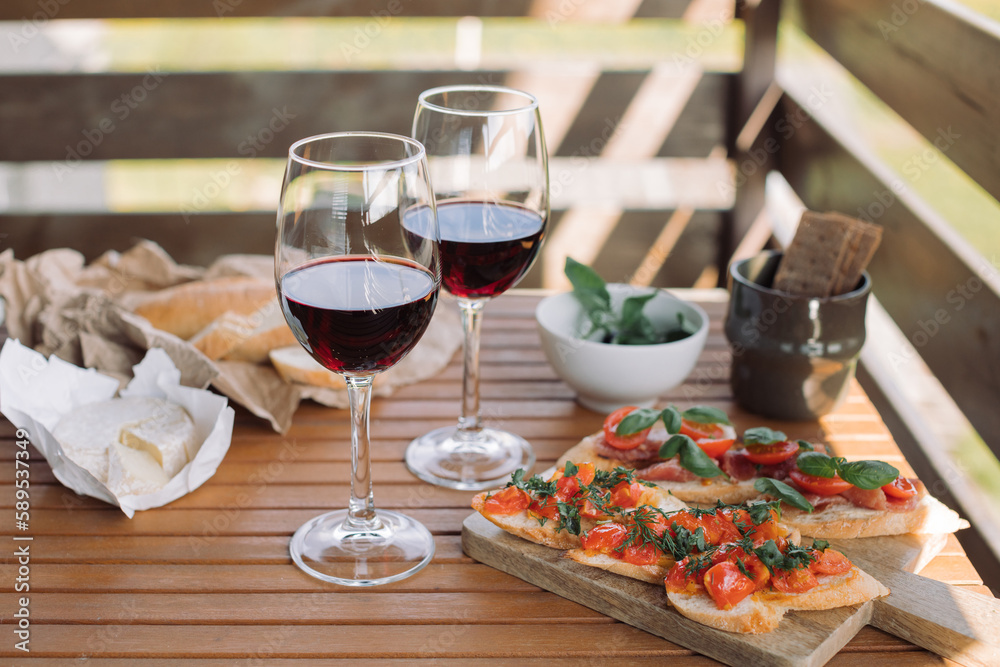 Glasses of wine, bruschetta with tomato and basil, cheese, olives. Table setting for relaxing at summer terrace on sunny day. Glasses of wine, bruschetta with tomato and basil, cheese, olives. Table setting for relaxing at summer terrace on sunny day.