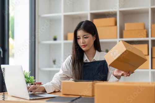 Startup SME small business entrepreneur of freelance Asian woman using laptop and box to receive and review orders online to prepare to pack sell to customers, online sme business ideas