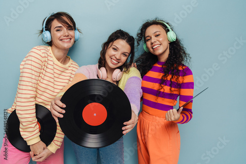 Three beautiful girls holding vinyl records and smiling isolated over blue background