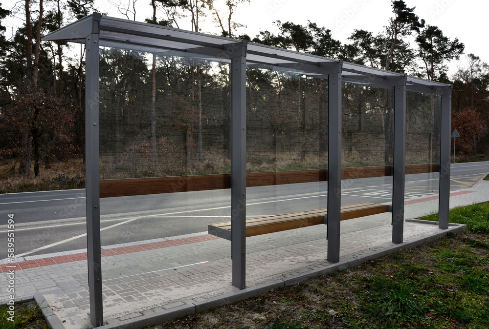 Fototapeta premium city bus stop. glass shelter with integrated wooden bench. only the roof and the back wall. on the street by the sidewalk in the city. elegant arch, station, platform, lawn, grass, tactile