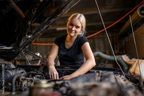young female australian tradesperson mechanic working on car engine in auto repair garage