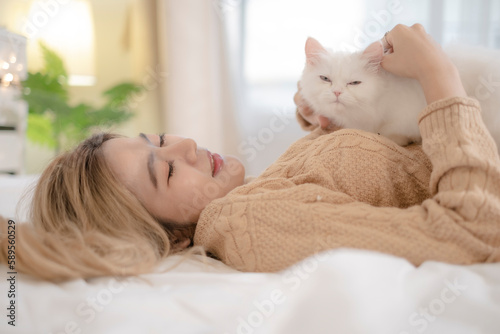 Cute fluffy kitten sitting on woman in brown sweater lay on bed with space of text, relationship with owner and pet.