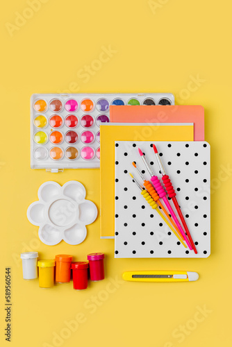 Various colorful material for creativity and art activity is arranged neatly on yellow background. Stationery and supplies for drawing and craft. Workplace organization.