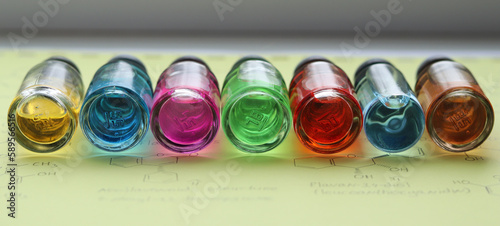 A row of seven glass bottles with colored solutions of organic dye compounds.