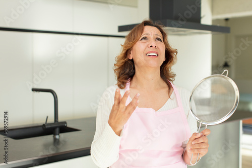 middle age pretty woman screaming with hands up in the air. cooking at home concept