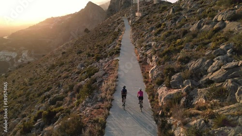 Sunset Ride.Two cyclists enjoying a scenic route along an empty mountain road in Spain with stunning views of the sunnset and mountains. Aerial drone video, follow shot. Alicante, Costa Blanca, Calpe photo