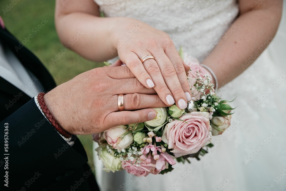 Closeup of bride and groom hands with rings on bouquet with roses Closeup of bride and groom hands with rings on bouquet with roses